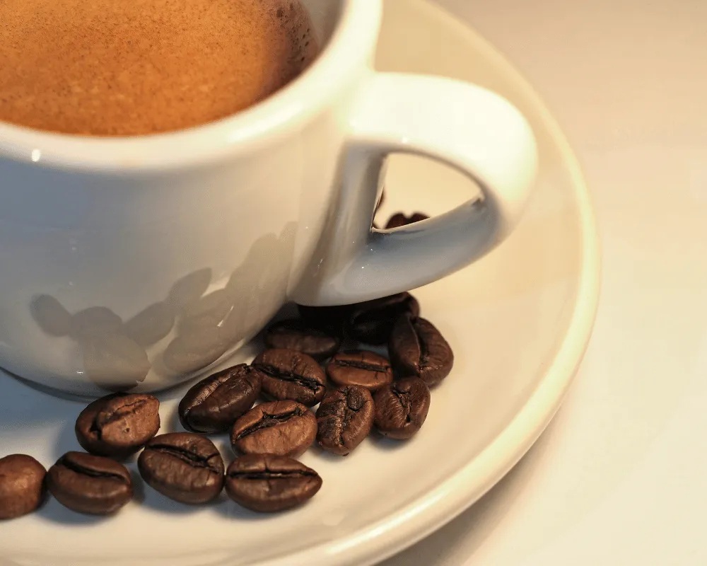 Taza de café espresso en una taza blanca con granos de café tostado sobre el plato, representando café en grano fresco.